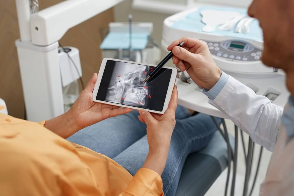 male dentist pointing at digital tablet with tooth X-ray image during consultation