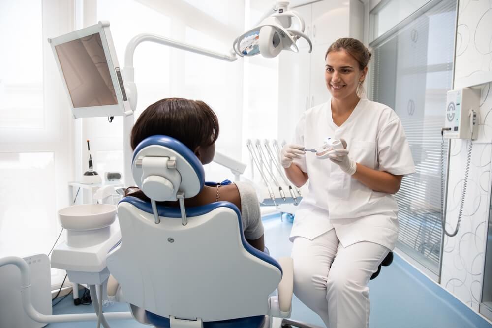 Smiling dentist teaching young female patient to clean teeth
