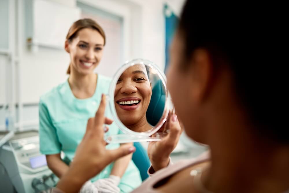 woman using mirror while looking at her teeth