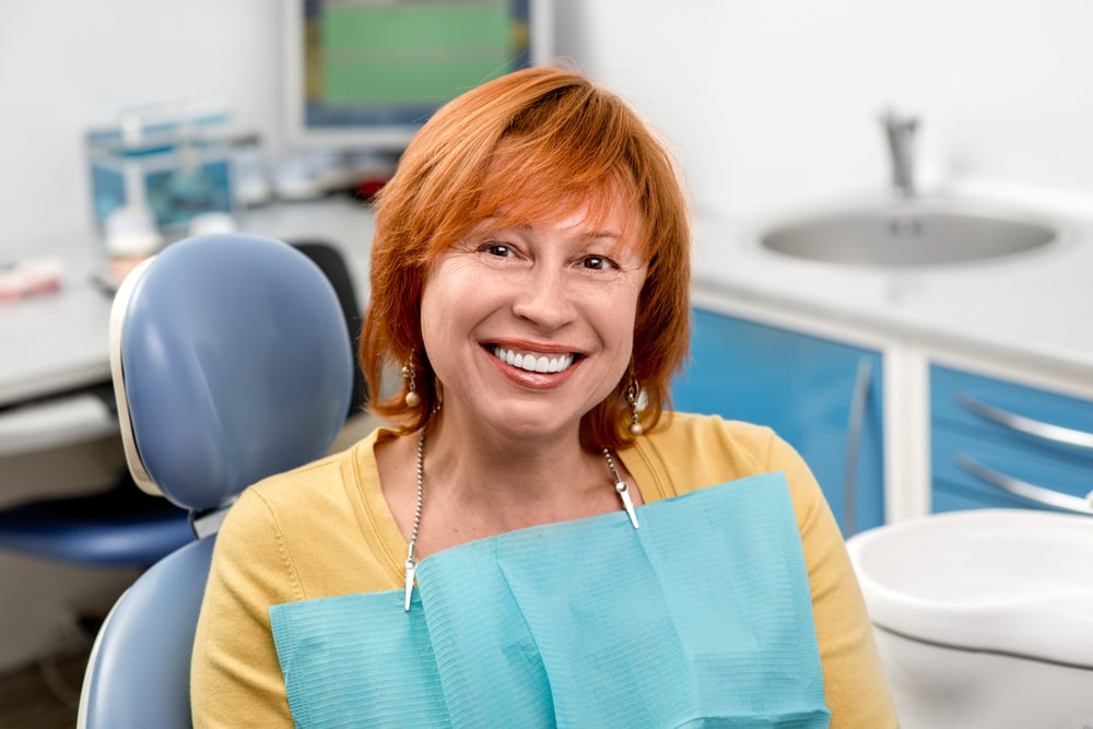 Smiling senior woman with new dental implants sitting in the dental office